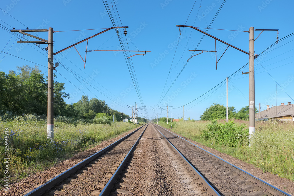 Double-track railway on a summer morning with the contact lines in rural areas