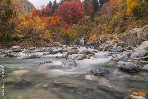 Landscape with a mountain river in the autumn forest on the mountain slopes at long exposure. Amanauz River in Dombai, Caucasus Mountains, Russia