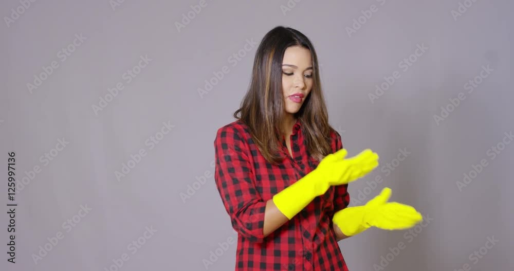 Attractive housewife holding up gloved hands in colorful yellow rubber gloves with a wry smile as she prepares to do the housework Attractive housewife holding up gloved hands in colorful yellow rubber gloves with a wry smile as she prepares to do the housework