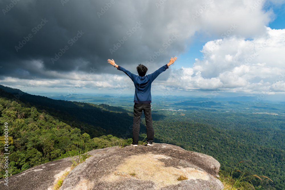 Young successful man open arms on mountain peak above the forest Young successful man open arms on mountain peak above the forest