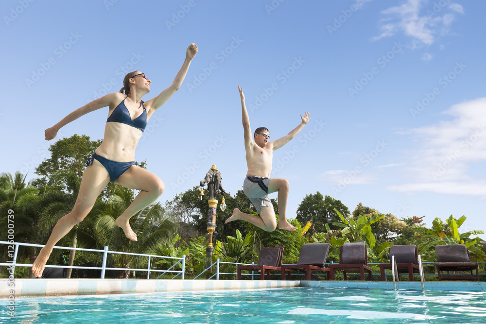 Two friends enjoy jumping in swimming pool, tropical resort, happiness