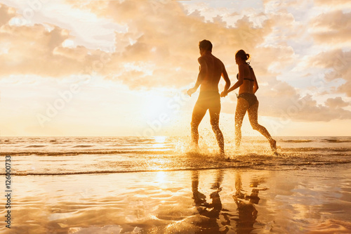 Happy cheerful couple running to the sea  water splashes  sunset