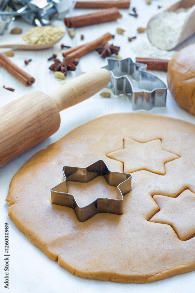 Making gingerbread cookies. Dough, metal cutter and rolling pen on wooden table, spices on background, vertical Making gingerbread cookies. Dough, metal cutter and rolling pen on wooden table, spices on background, vertical