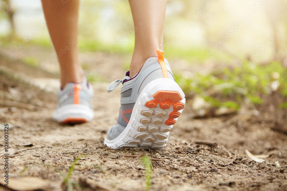 Rear shot of athletic legs of woman jogger pink running shoes during jogging exercise outdoors. Female runner hiking on trail forest on sunny day getting prepared for marathon Stock-foto