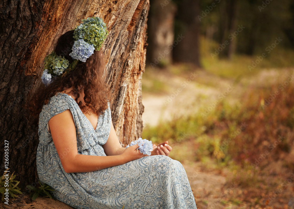 Kobieta w wianku na głowie siedząca pod drzewem - obrazy, fototapety, plakaty 