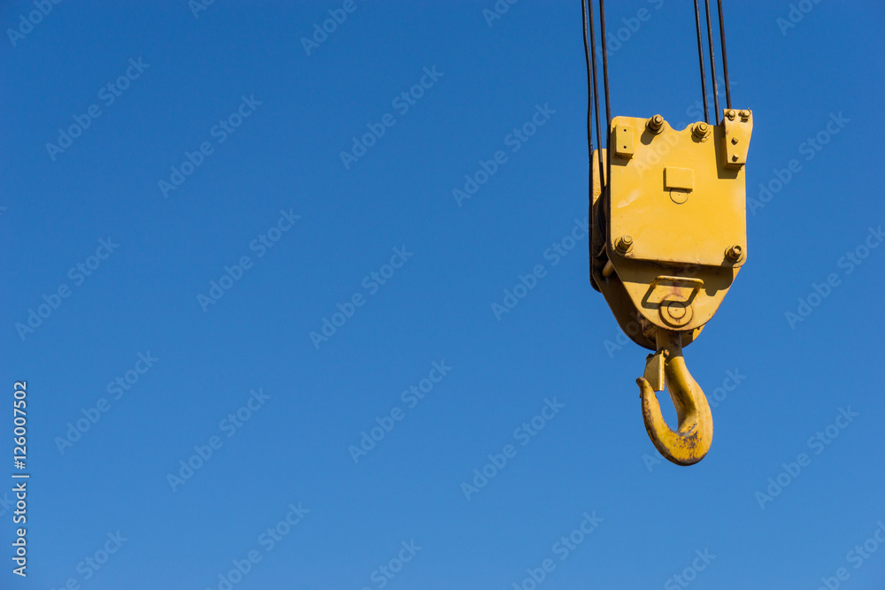 A yellow crane hook suspended against a blue sky A yellow crane hook suspended against a blue sky