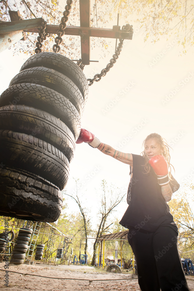 Woman boxer with tatto arms at workout. Young woman is boxing punching bag  from car tires. At the head of the girl dreadlocks. Toned photo. Stock  Photo | Adobe Stock