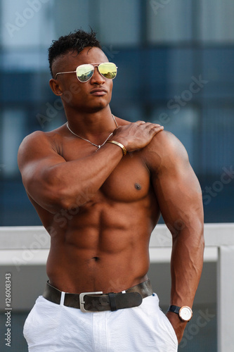 Hot Beautiful black guy with bulging muscles posing against the backdrop of the urban landscape Man fitness model with a beautiful body on the background of the city Shirtless Hunk man without a shirt