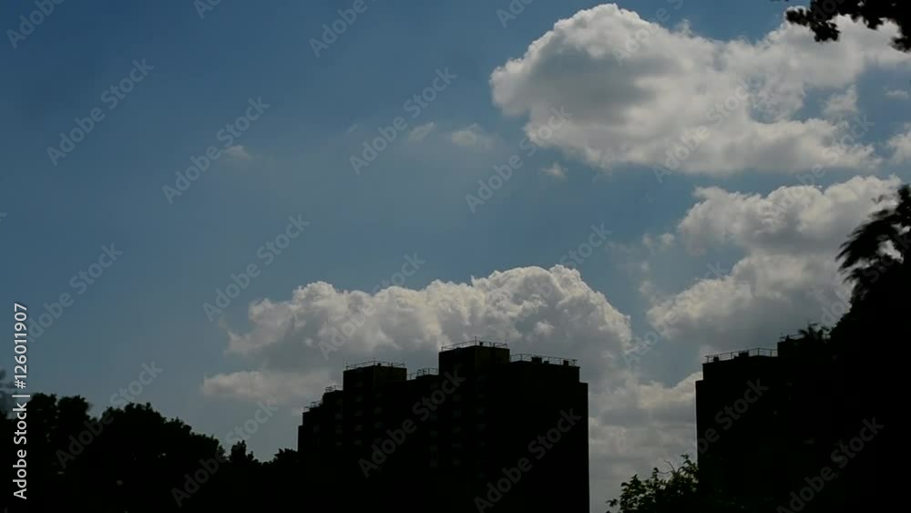 Time lapse of scenic white cumulus clouds bubbling and boiling above silhouettes of apartment block buildings and trees Time lapse of scenic white cumulus clouds bubbling and boiling above silhouettes of apartment block buildings and trees