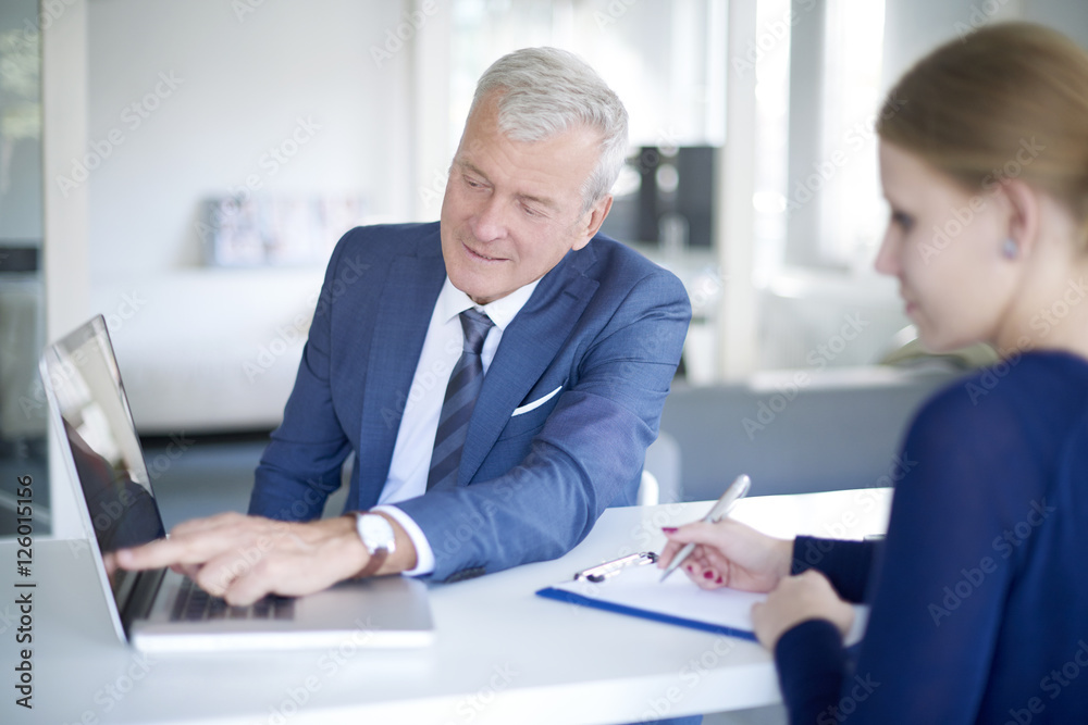 Fototapeta premium Financial team at work. Shot of a senior investment advisor businessman consulting with her young assistant while sitting at office and working on laptop.