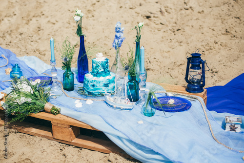 Scenery for taking photos in nautical style. Cake, candles, seashells, bride's bouquet on a sandy beach. Marine wedding themes