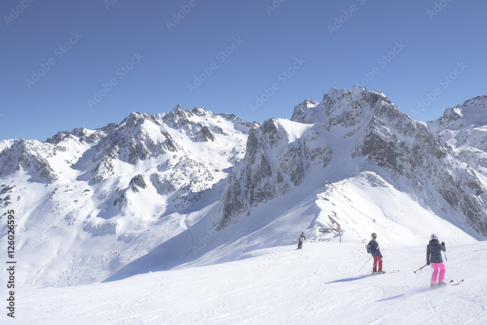Unidentified skiers are on the snowy slope into  Grand Tourmalet ski resort against the mountain range in the French Pyrenees