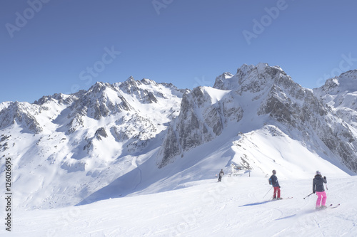 Unidentified skiers are on the snowy slope into Grand Tourmalet ski resort against the mountain range in the French Pyrenees