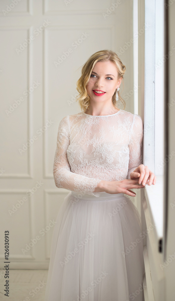 Beautiful bride standing at window in white room. Beautiful bride standing at window in white room.