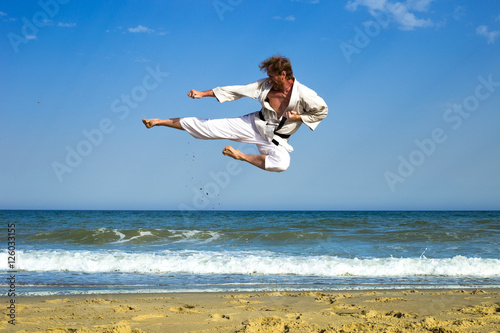 Adult man practicing a kata and kicks on the beach