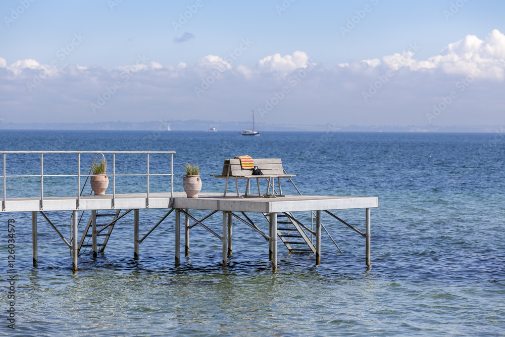 Jetty with stairs into the sea with recreational bench towel and purse 