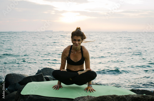Young woman practicing yoga at rocky seashore at sunrise or sunset