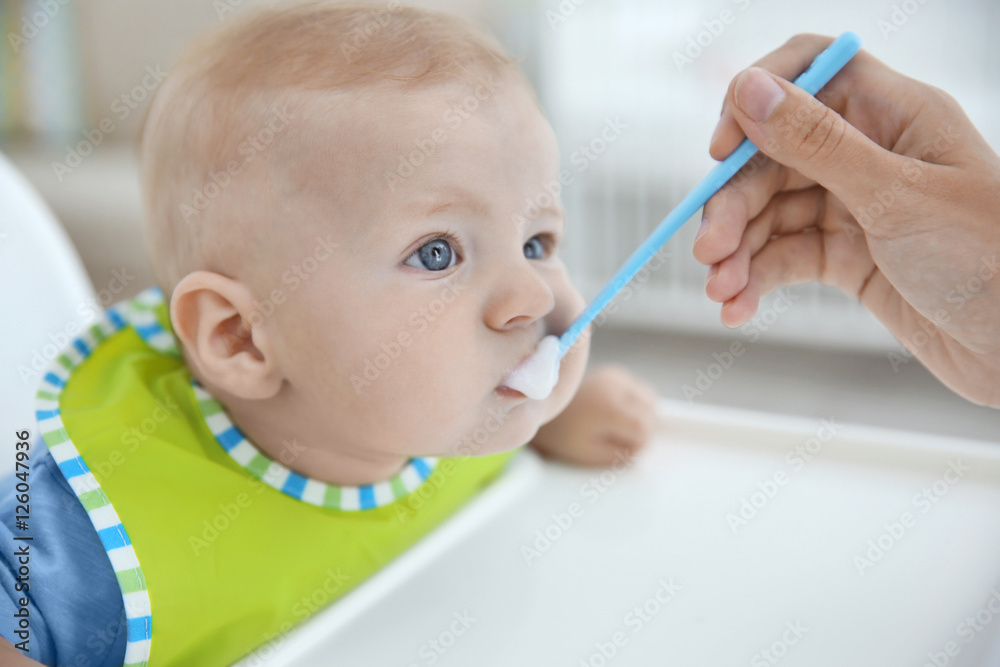 Mother feeding baby with spoon indoors Mother feeding baby with spoon indoors