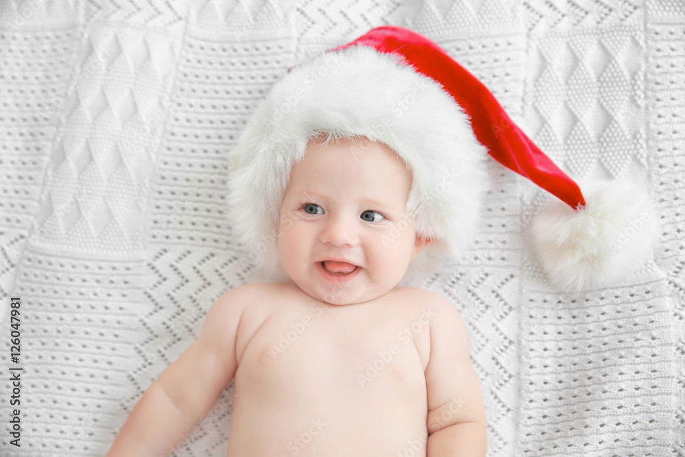 Little baby in Christmas hat on white bed Little baby in Christmas hat on white bed
