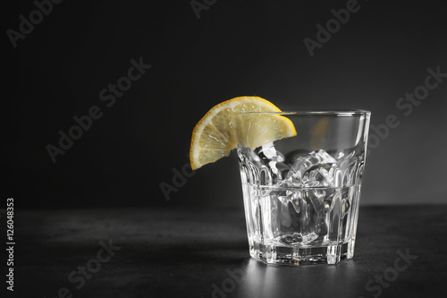 Glass of vodka with lemon and ice on dark background