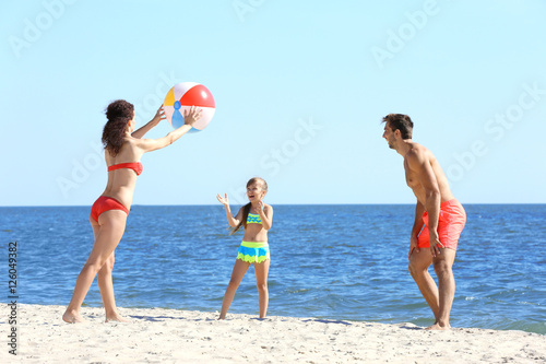 Family concept. Parents and daughter playing with ball on the beach