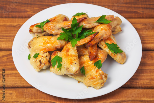 Plate with baked chicken wings and parsley on a wooden background