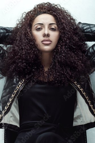 Fashion portrait of a beauty brunette girl with curly hair in leather jacket.
