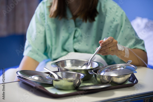 Patient woman is on drip receiving a saline solution with cooked rice and other food in stainless bowl