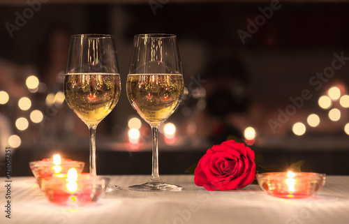 Romantic dinning concept. Pair of wine glasses on a table next to red rose. 