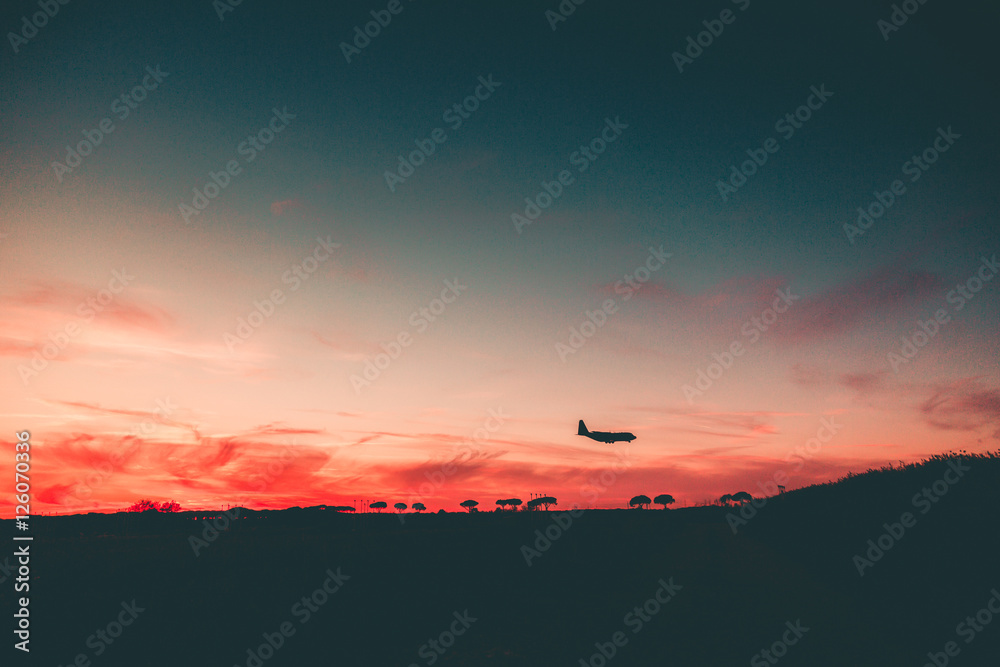 Beautiful sunset with a Silhouette of an Airplane approaching at the Airport. 