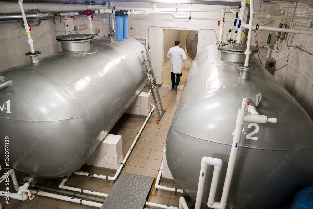 Horizontal storage tanks. Man in a white coat. Chief engineer checks equipment. Water purification at the plant. Horizontal storage tanks. Man in a white coat. Chief engineer checks equipment. Water purification at the plant.