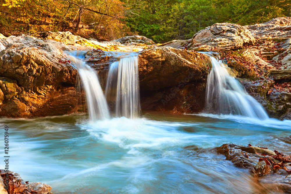 Beautiful waterfall in forest at sunset. Autumn landscape, fallen leaves, water flow 
