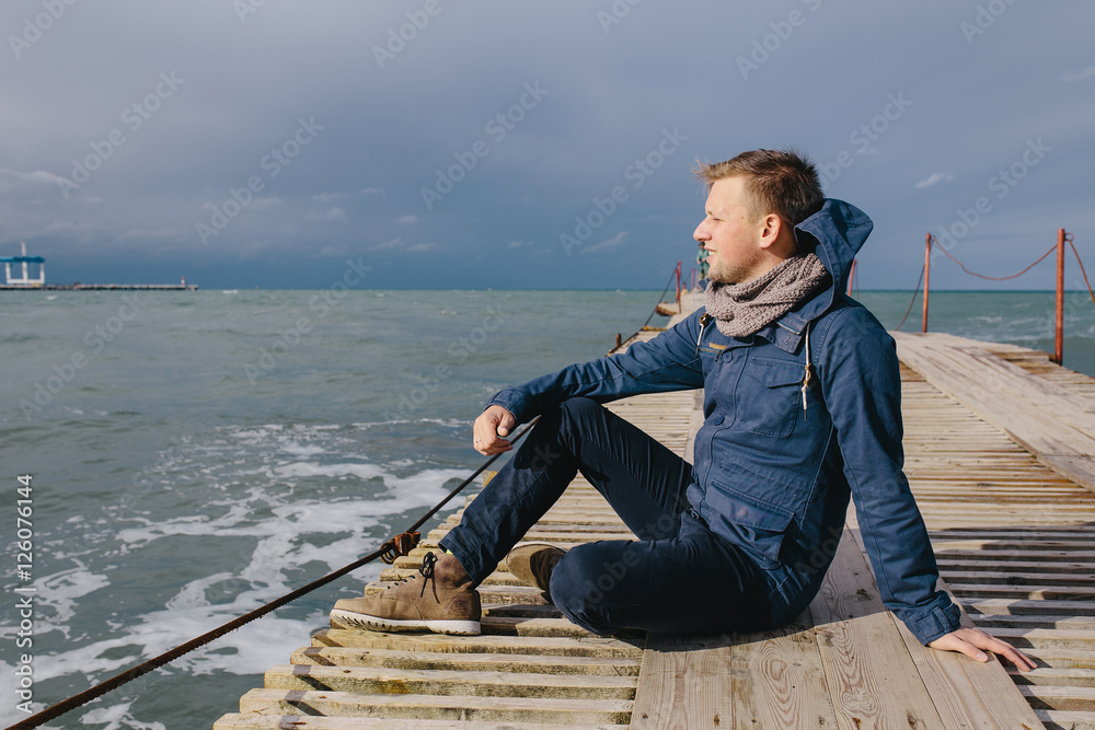 young man sitting on a wooden pier on the background of stormy sea