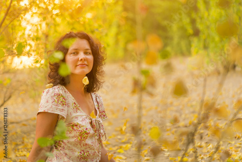 Adult brunette woman in a dress throws up dry yellow leaves in the autumn forest, sunny