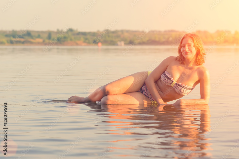 Obraz premium Blonde beautiful woman in a swimsuit lying in the water at sunset or sunrise