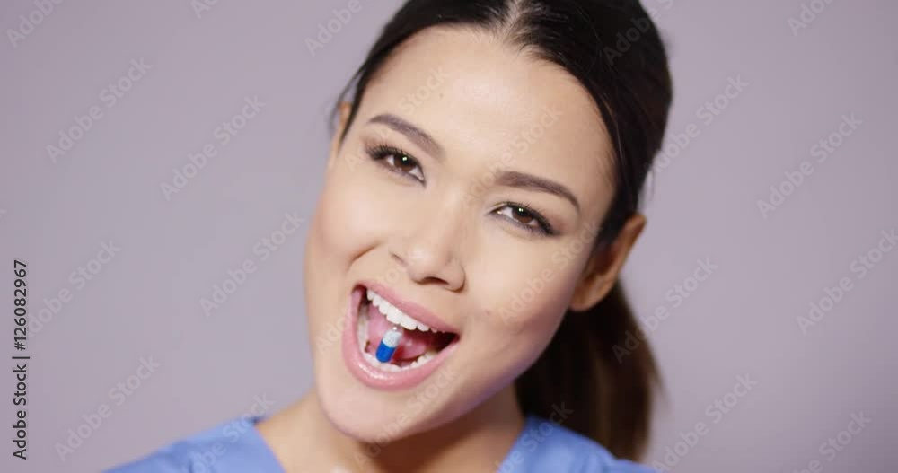 Pretty young woman taking her medication showing a blue and white capsule on her tongue with a smile close up head shot Pretty young woman taking her medication showing a blue and white capsule on her tongue with a smile close up head shot
