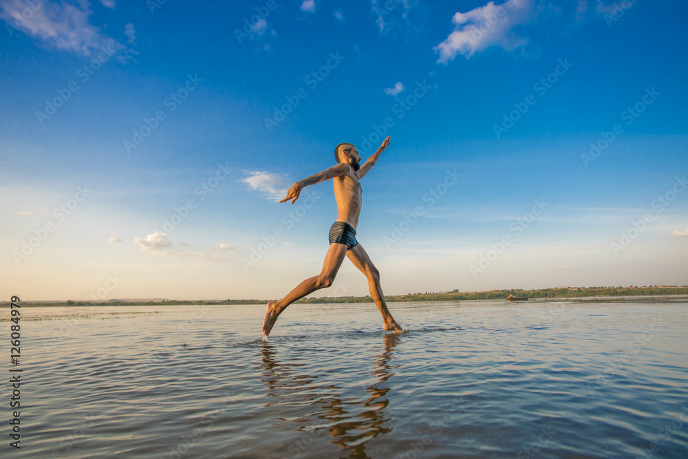 Adult man with a mohawk on his head and black shorts running on water against the backdrop of blue sky with clouds