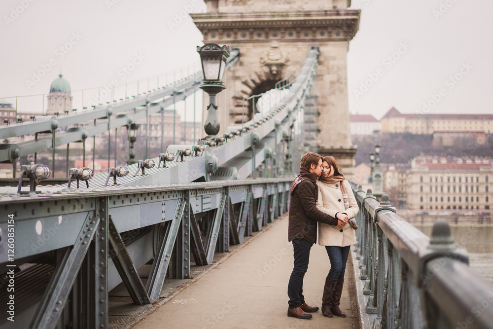 Fototapeta premium Christmas in old town. Young cheerful caucasian couple in warm cozy clothes walking in city centre.