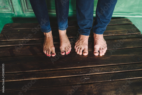 Closeup of female and male bare feet in jeans on wooden floor
