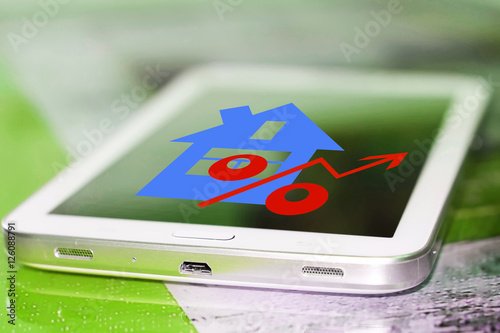 Red percentage sign and house on your phone screen . The concept of online sales of real estate . photo