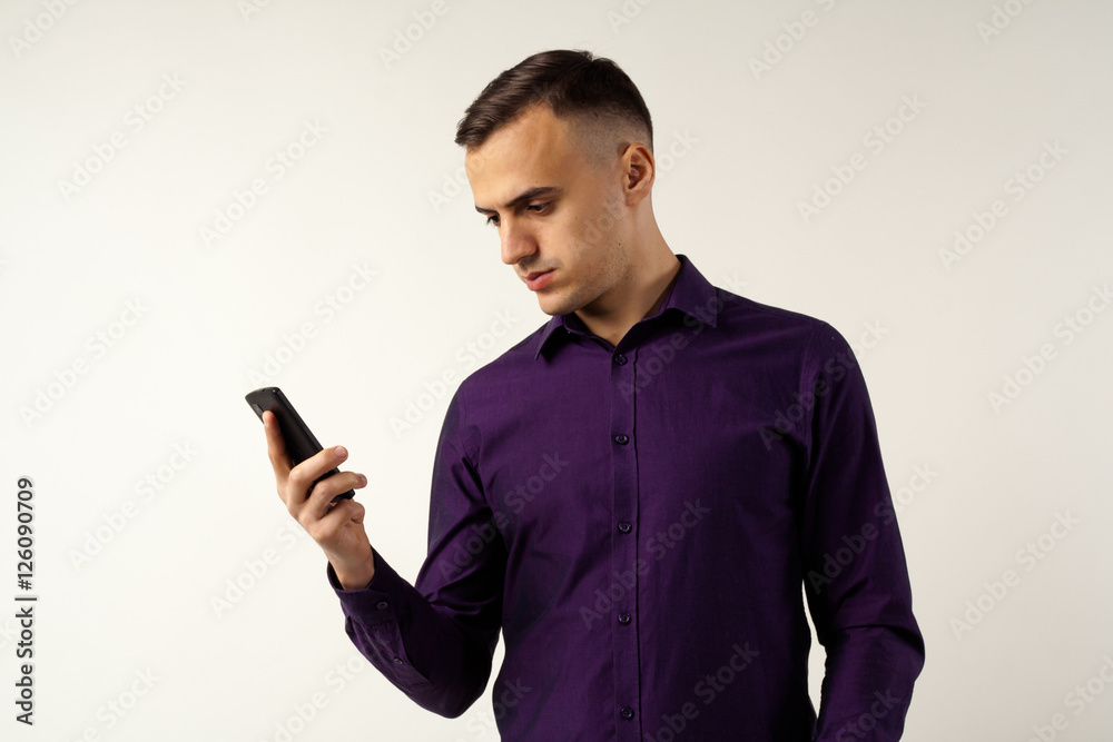 The young man looks at a mobile phone and reads or writes a message. He is calm, he is a successful businessman or just an office worker.