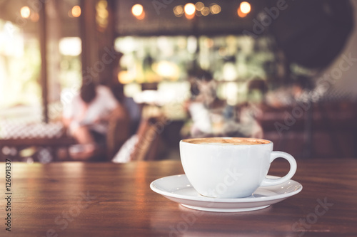 Filiżanka gorąca kawa na stole w kawiarni z ludźmi. efekt kolorystyczny vintage i retro - płytka głębia ostrości