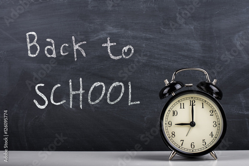 Retro alarm clock and text "Back to school" written with chalk on the blackboard.