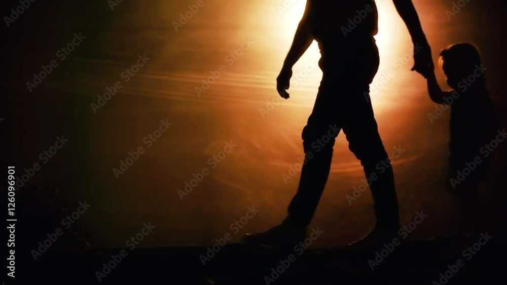 Low section of silhouettes of father and daughter walking against desert-like background in darkly lit studio Low section of silhouettes of father and daughter walking against desert-like background in darkly lit studio