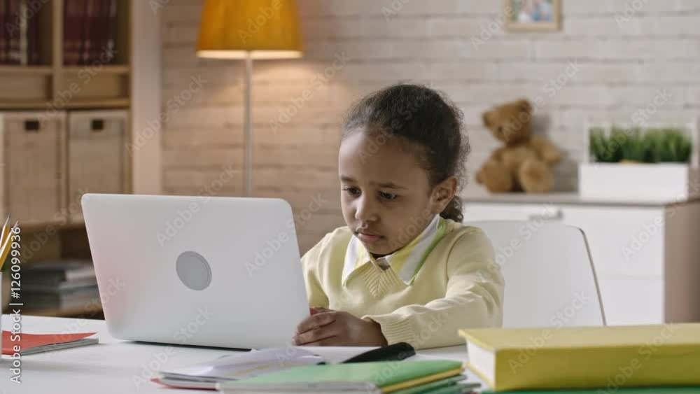 Concentrated little girl working on modern laptop at the table in her room Concentrated little girl working on modern laptop at the table in her room