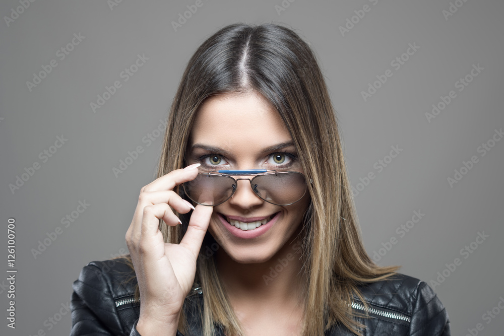Portrait of smiling green eyed beautiful young woman holding sunglasses glance at camera over gray studio background Portrait of smiling green eyed beautiful young woman holding sunglasses glance at camera over gray studio background