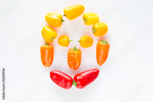 Peperoni rossi gialli e arancioni raffiguranti un viso umano su fondo chiaro photo