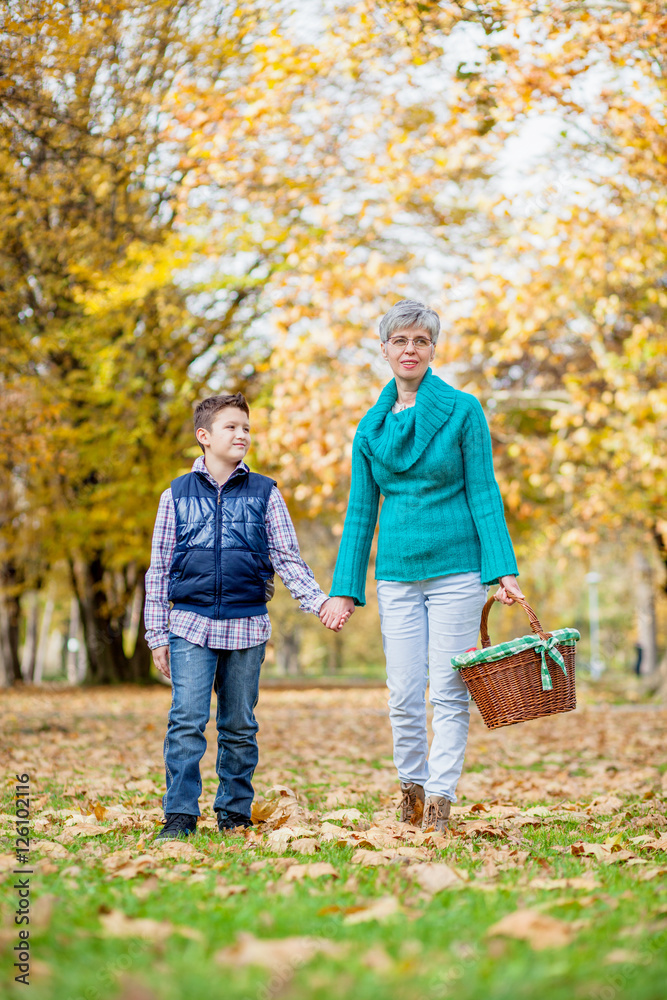 Grandmother and grandson take a walk during the fall of the leaves in the park 