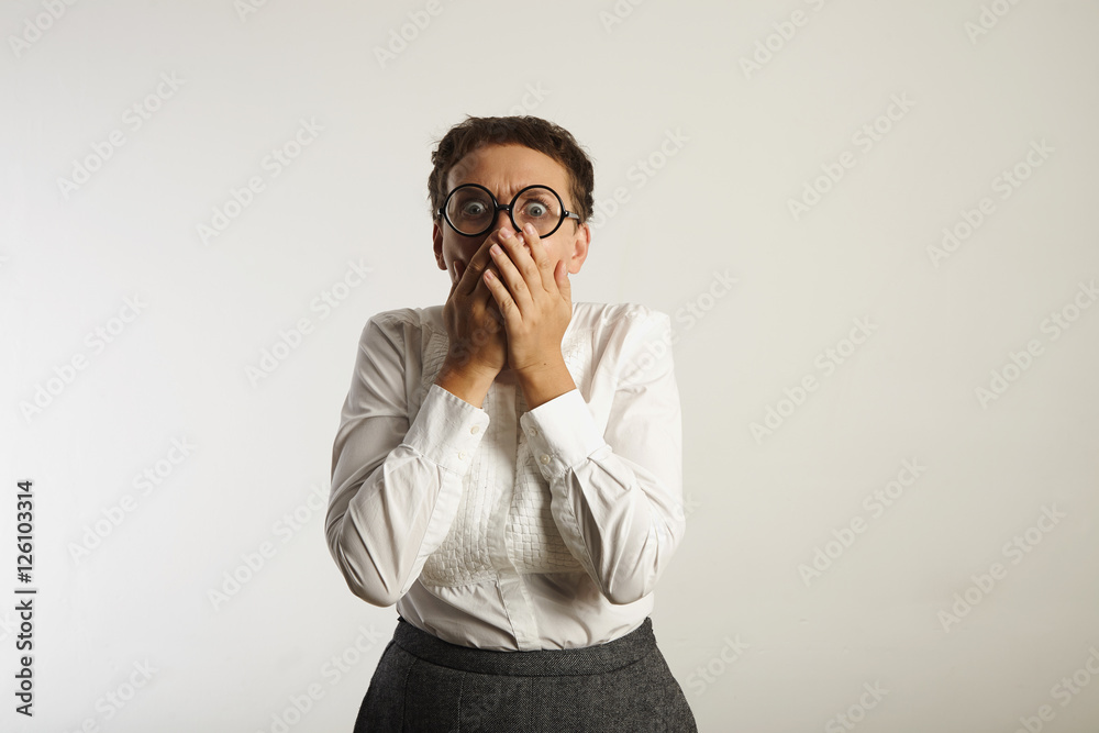 Frightened teacher in white blouse and grey skirt covers her mouth with her hands and screams looking into the camera Frightened teacher in white blouse and grey skirt covers her mouth with her hands and screams looking into the camera