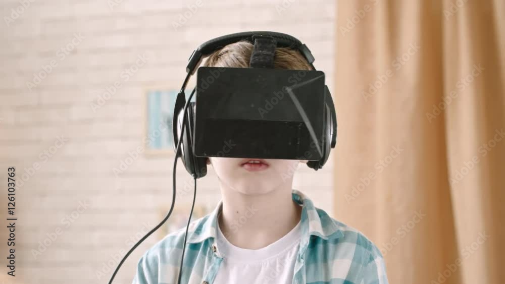 Closeup of little boy with black virtual reality headset standing in the room at home Closeup of little boy with black virtual reality headset standing in the room at home